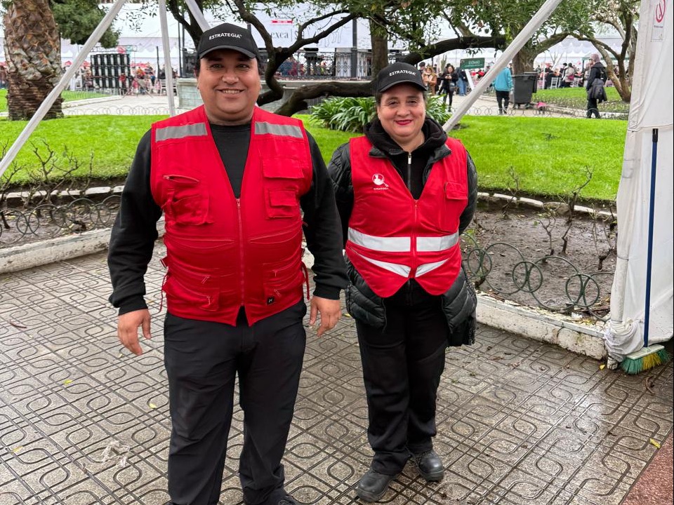 Dos guardias de Estrategia Security con chaleco rojo reflectante y gorra en el acceso del recinto de la Fiesta Costumbrista del Chancho de Talca 2026, con público al fondo