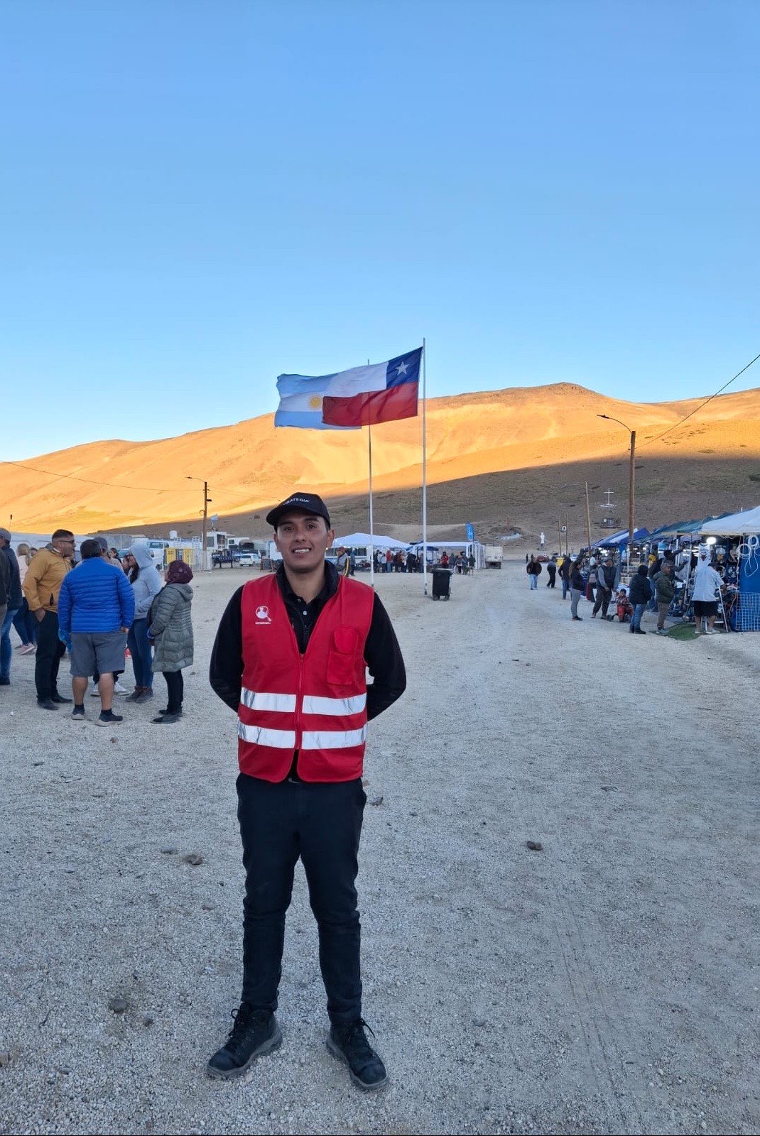 Guardia de Estrategia Security con chaleco reflectante en el recinto del encuentro binacional del Paso Fronterizo Pehuenche, con las banderas de Chile y Argentina y la cordillera al fondo